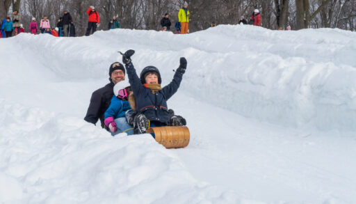 Family having fun sledding down a snowy hill.