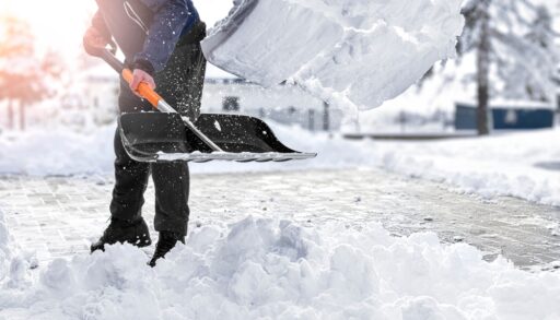 Close-up of someone shovelling snow from their driveway with a black shovel.