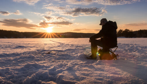 Silhouette of a man ice fishing at sunset.