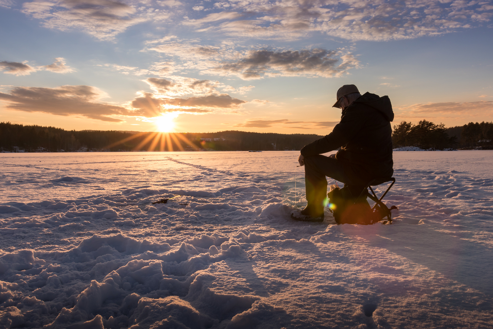 Silhouette of a man ice fishing at sunset.