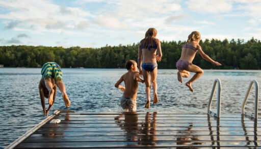 Four kids jumping off a dock into a lake.