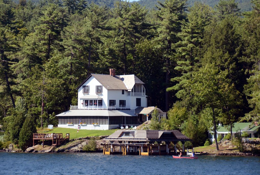 A large white, lakeside home surrounded by trees.