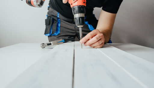 Person screwing a screw into a white board.