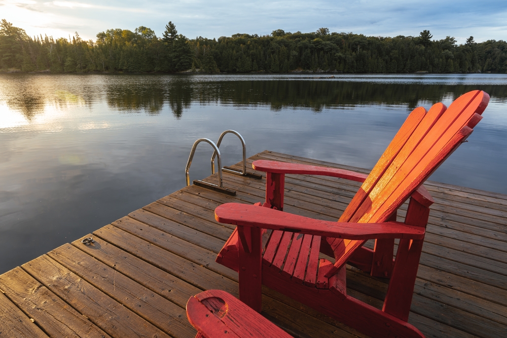 Two red chair facing a sunset on a dock overlooking a lake.