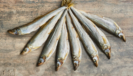 Eight rainbow smelt fish on a wooden board.