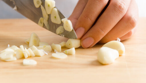 Person cutting garlic clove on a wooden cutting board.