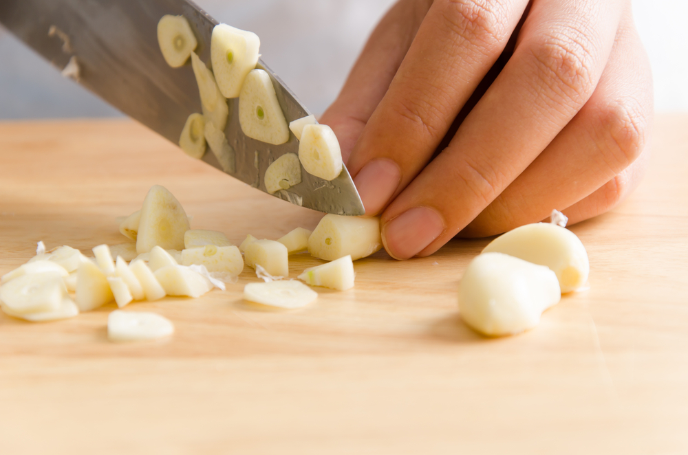Person cutting garlic clove on a wooden cutting board.
