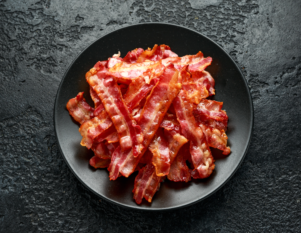 Pile of cooked bacon on a black plate.