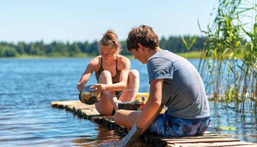 A young woman and a boy washing dishes in a lake.