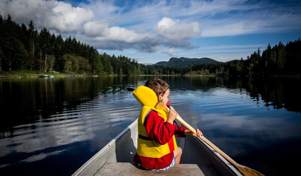 Little kid sitting in a canoe, paddling.