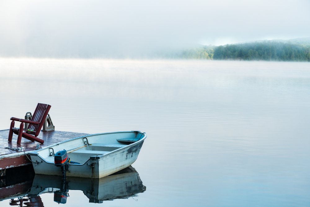 An old boat next to a wooden dock on a still, misty lake.