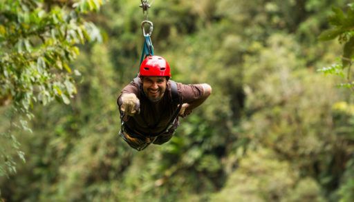A man wearing a red helmet smiling as he rides a zipline.