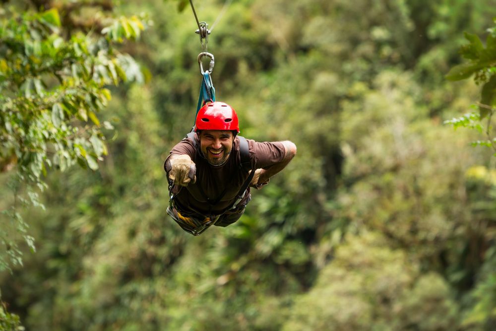 A man wearing a red helmet smiling as he rides a zipline.