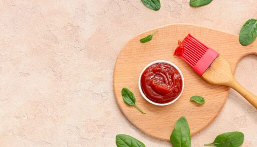 Top view of a dish of barbecue sauce next to a red silicone brush.