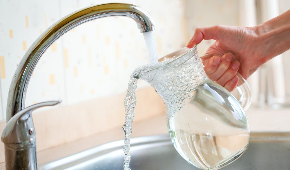 Close-up of a person filling a glass pitcher with tap water.