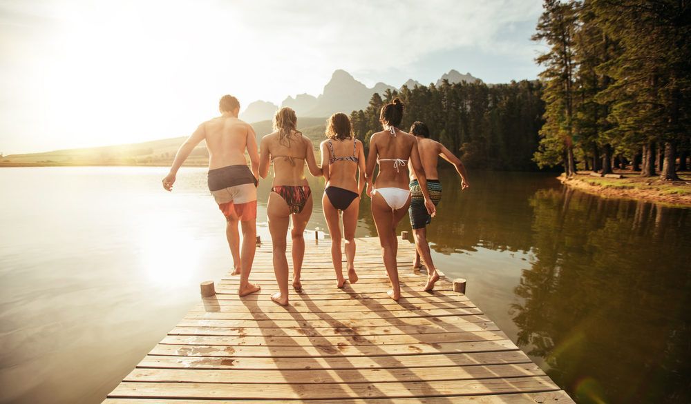 A group of friends jumping off a dock at the lake.