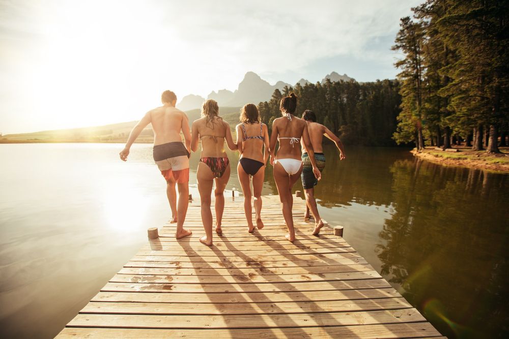 A group of friends jumping off a dock at the lake.
