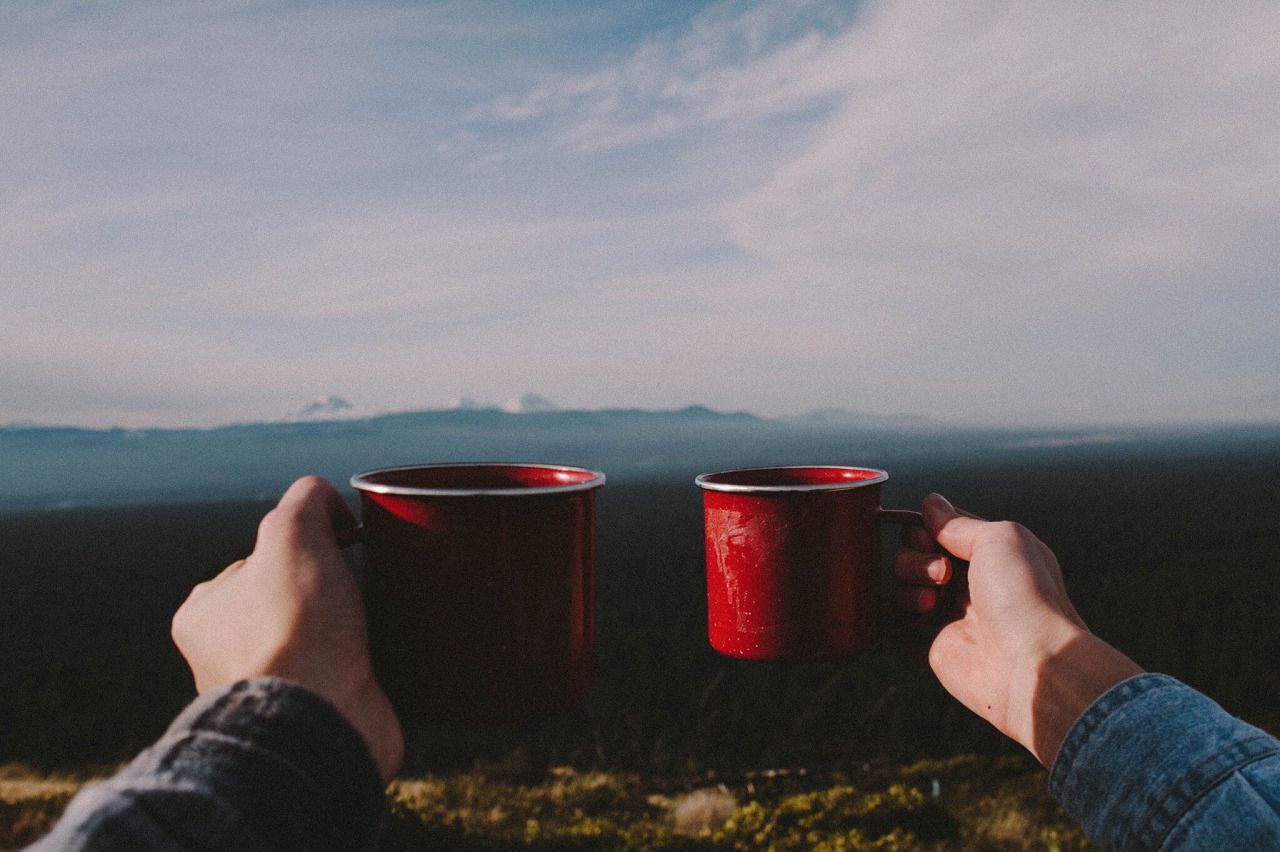 people holding enamel cups in front of mountain view