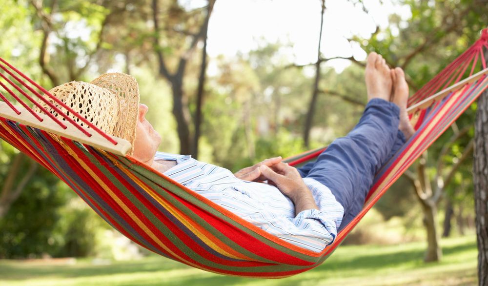 Person wearing a straw hat laying in a red, green, and yellow striped hammock.