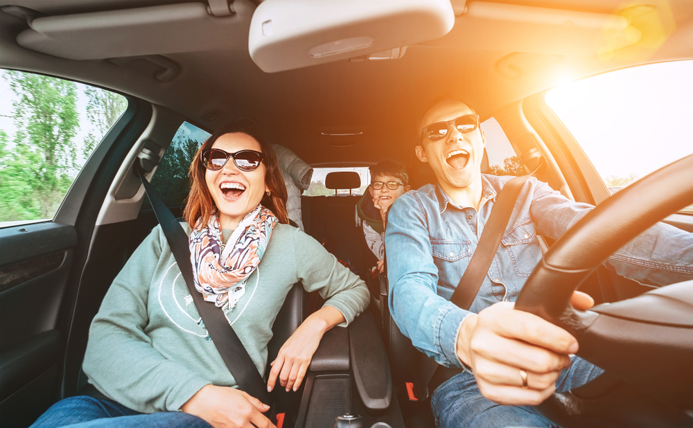 Couple and a child singing in a car on a road trip.