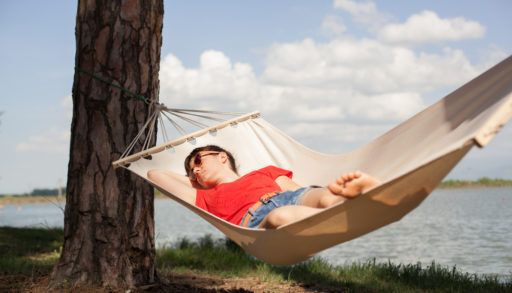Person in a red shirt laying in a hammock by a lake.