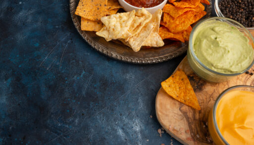Assorted chips with dips on wooden boards against a dark stone background.