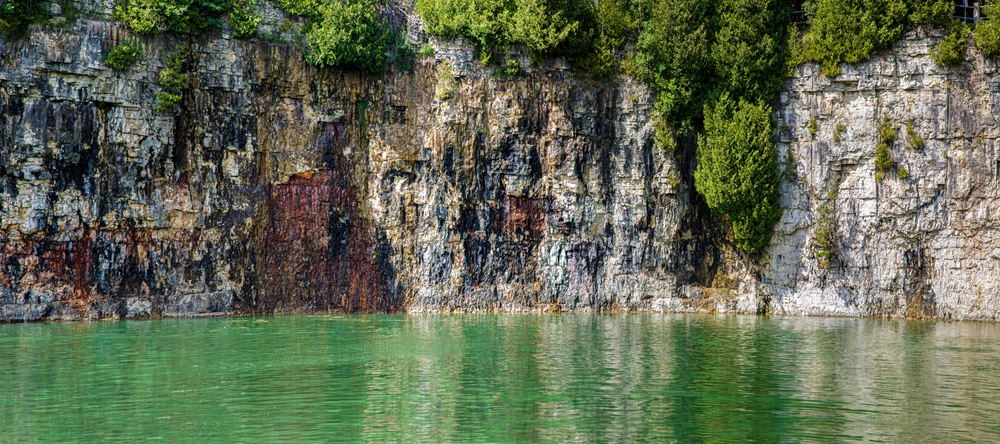 Green and rocky cliffs and calm waters of Elora Quarry Ontario, Canada.
