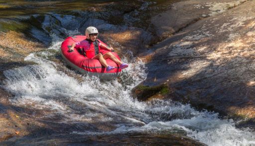 Kid tubing in a red tube in a river.