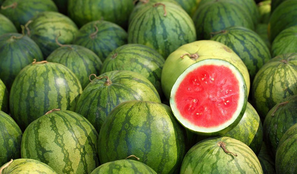 Open half of a watermelon sitting on top of more watermelons.