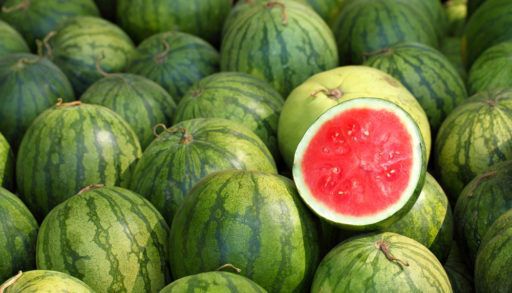 Open half of a watermelon sitting on top of more watermelons.