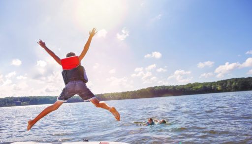 Kid in a red life jacket jumping into a lake.