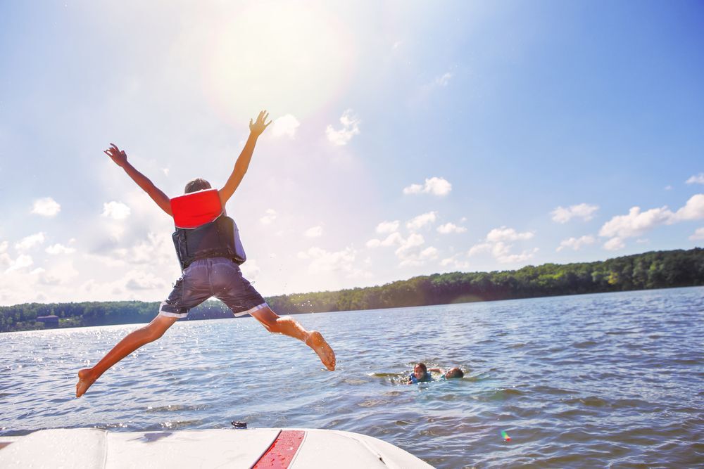 Kid in a red life jacket jumping into a lake.