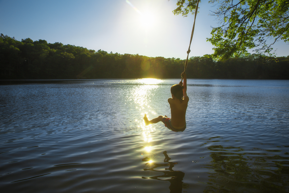 Boy swinging into a lake on a rope swing at sunset.