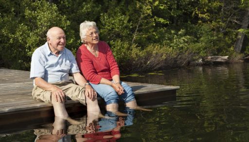 Older couple sitting on a wooden dock with their feet in the water.