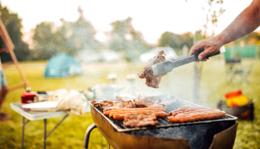 Person grilling hot dogs and burgers in a park.