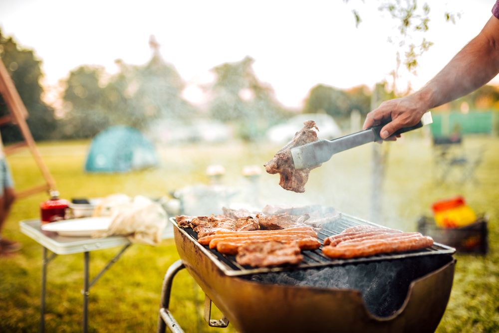 Person grilling hot dogs and burgers in a park.