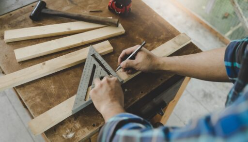 Person in a blue plaid shirt measuring out wood to cut.