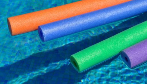 Coloured pool noodles floating in a pool.