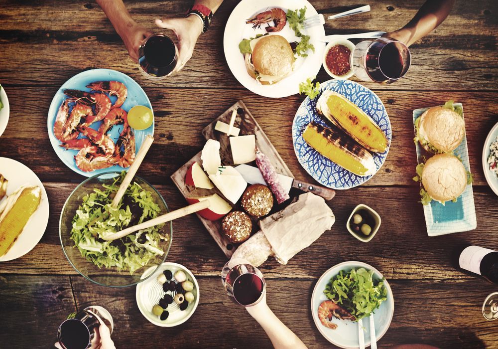 Bird's-eye-view of a wooden table filled with food with the occasional hand reaching for something.