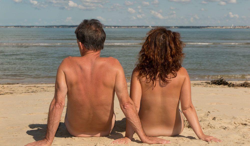 Couple sitting naked on a nude beach.