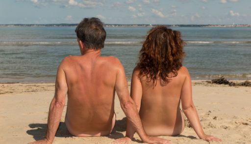 Couple sitting naked on a nude beach.