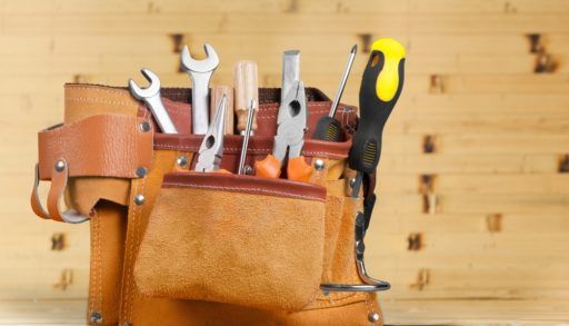 Tool belt filled with tools sitting on a wooden workbench.