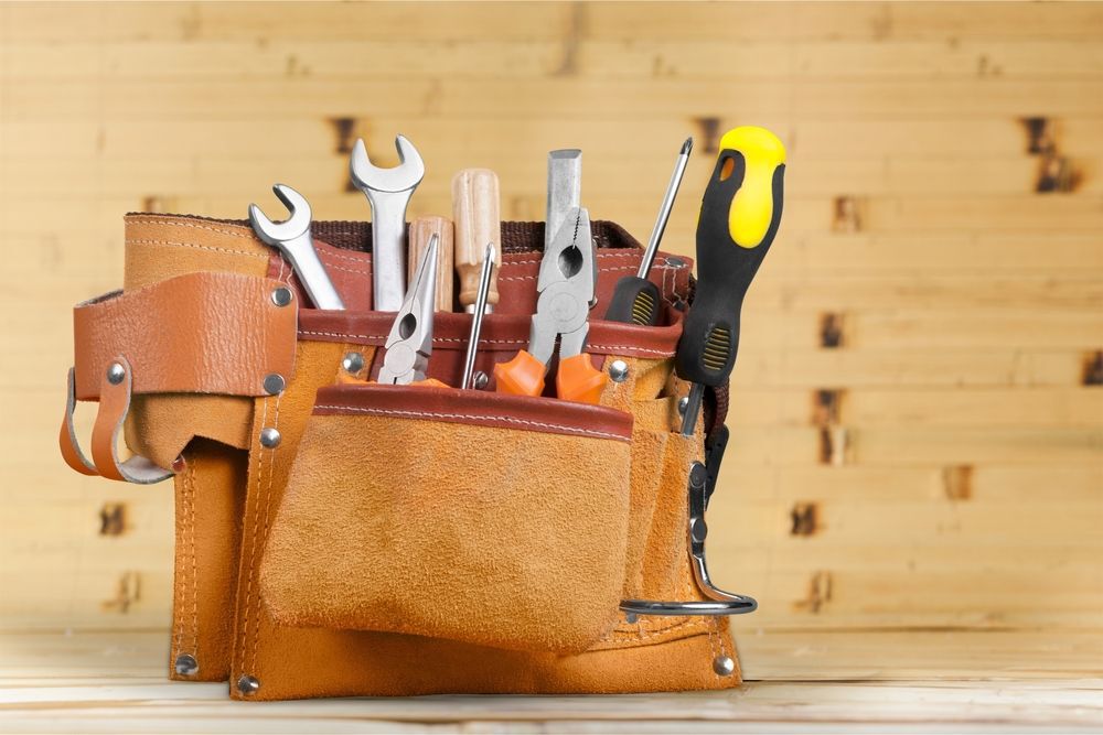 Tool belt filled with tools sitting on a wooden workbench.