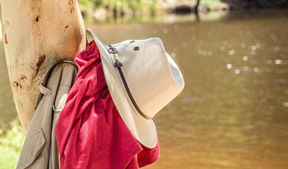 Red shirt and a beige hat and pants hung on a tree next to a river.