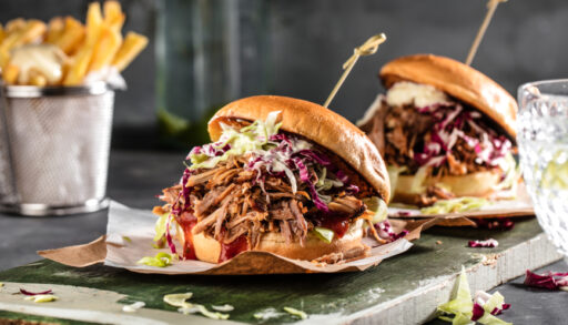Two homemade pulled pork sandwiches with coleslaw on top and a toothpick to hold it together.