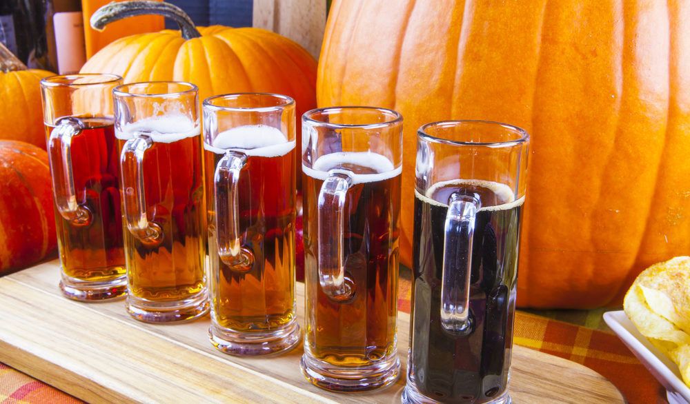 Beer flight on a wooden board in front of orange pumpkins.
