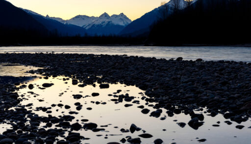 Mount Meager at sunset surrounded by silhouetted trees and a lake.