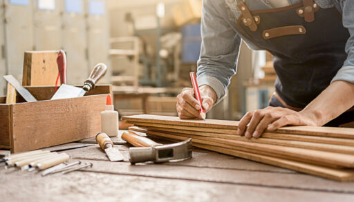Man in a grey apron measuring wood to be cut.