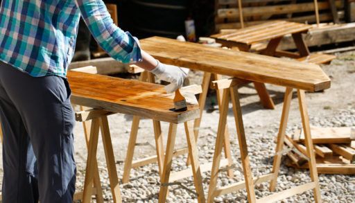 Worker in blue plaid applying stain to wood.
