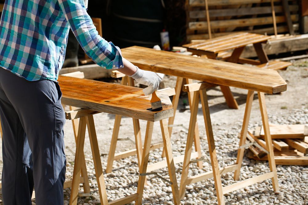 Worker in blue plaid applying stain to wood.